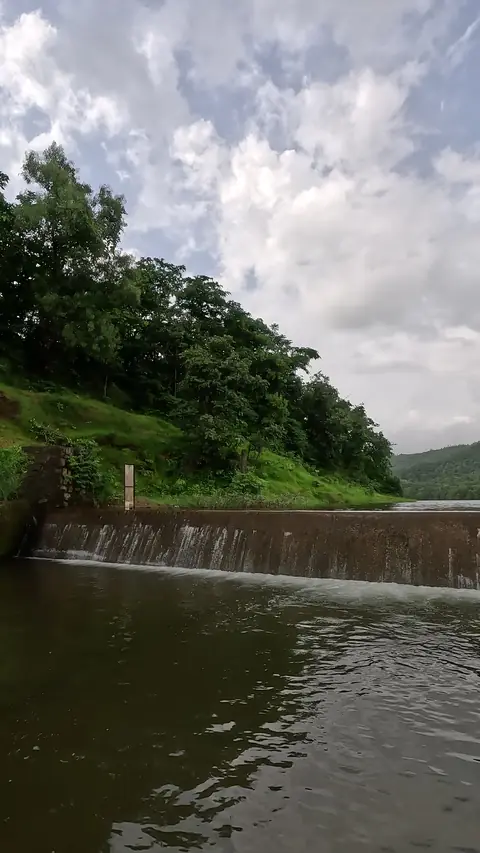 Water flowing over the Harkul Dam wall with hills behind, Kankavli